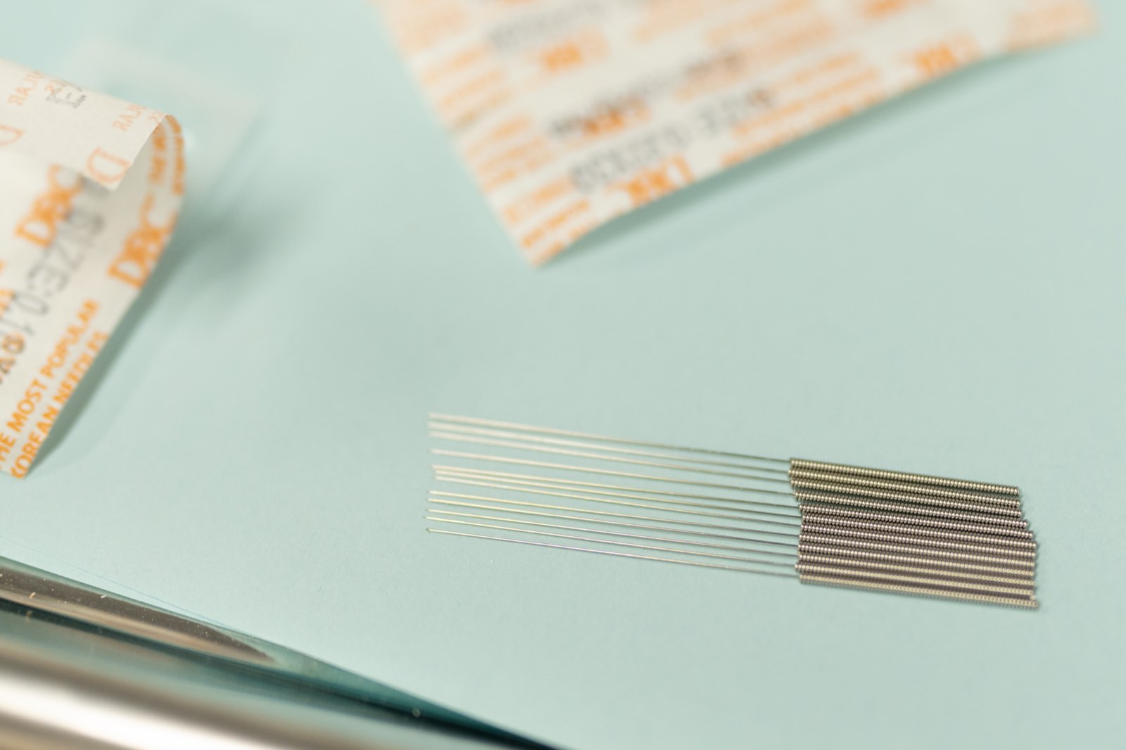 Close-up of sterile, single-use acupuncture needles next to their sealed packaging