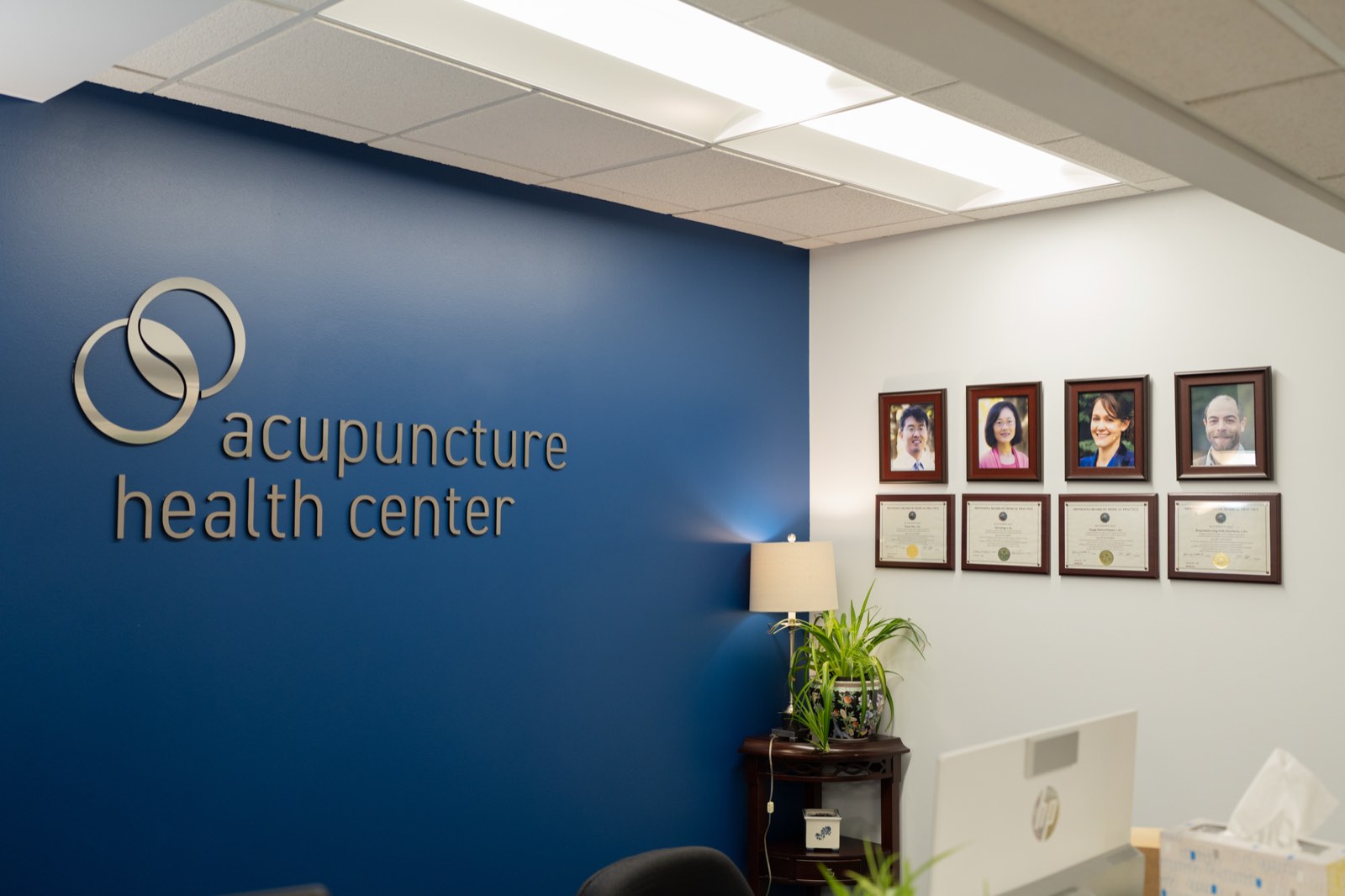 Clinic logo wall beside framed portraits and licenses of the practitioners