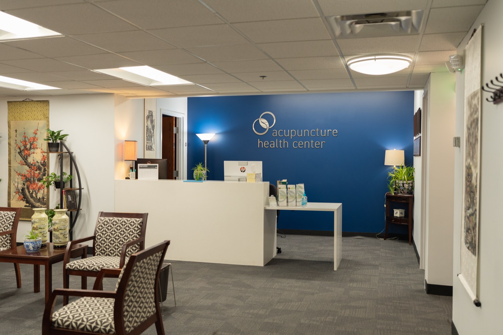 Reception area of Acupuncture Health Center with front desk, seating, and the clinic logo on a blue wall