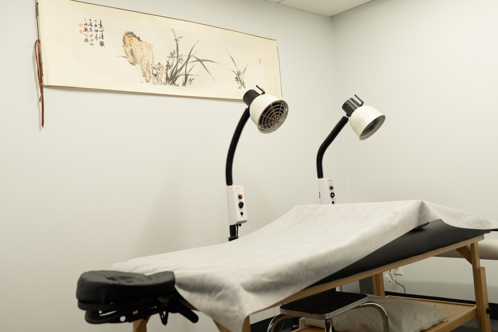 Treatment table with warming heat lamps beneath a traditional Chinese painting